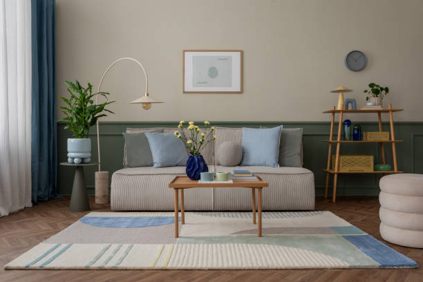 istock Creative composition of cozy living room interior with mock up poster frame, modular sofa, blue pillows, wooden coffee table, patterned rug, beige wall and personal accessories. Home decor. Template. 2163403524