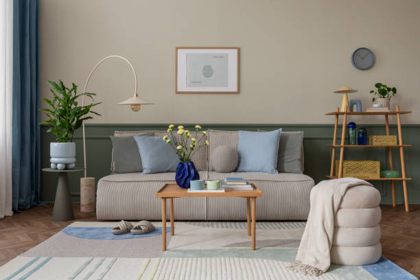 istock Creative composition of cozy living room interior with mock up poster frame, modular sofa, blue pillows, wooden coffee table, patterned rug, beige wall and personal accessories. Home decor. Template. 2163403564