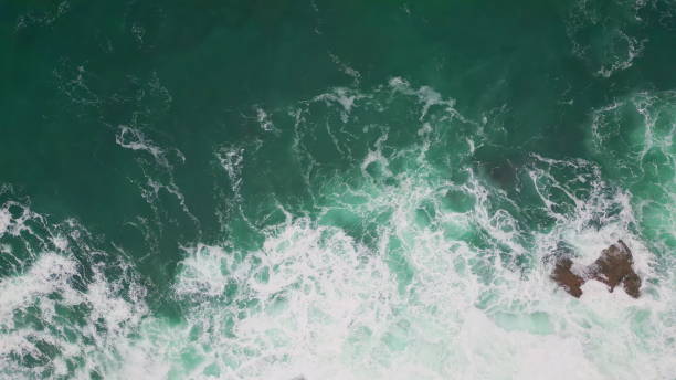 istock Sea washing rocky shore top view. Azure waves foaming splashing rough cliffs 2163410840