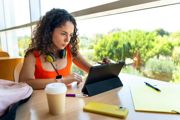 istock Young curly-haired girl studying with a tablet in the university library 2163411339