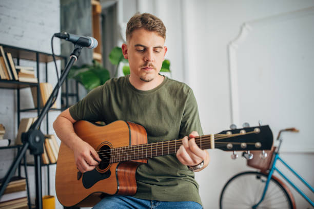 istock Focused man playing guitar with a microphone nearby. 2163415195