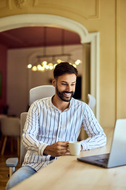 istock A smiling man working online while holding a cup of coffee, using a laptop. 2163415439