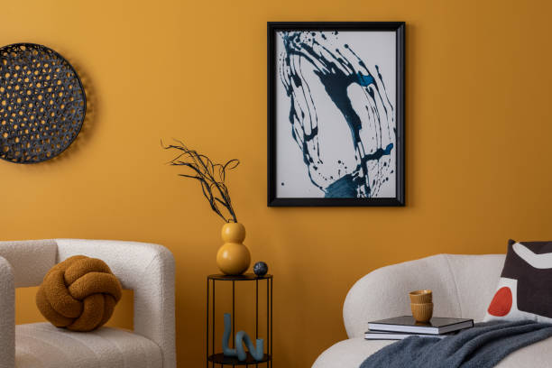 istock Cozy composition of warm living room interior with mock up poster frame, boucle sofa, patterned pillows, lamp, black rack, yellow wall, books and personal accessories. Home decor. Template. 2163417810