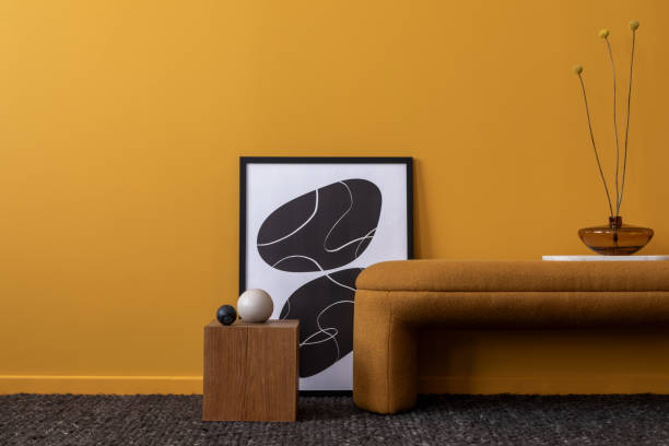 istock Creative composition of living room interior with mock up poster frame, orange bench, yellow wall, stylish sculpture, stand, vase with dried flowers and personal accessories. Home decor. Template. 2163417863