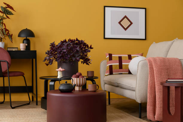 istock Warm and cozy living room interior with mock up poster frame, beige sofa, round coffee table, plaid, black desk, vase with flowers, chair and personal accessories. Home decor. Template. 2163420281