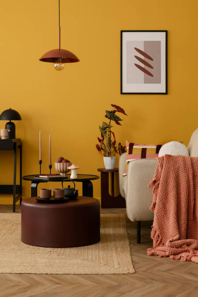 istock Warm and cozy living room interior with mock up poster frame, beige sofa, round coffee table, plaid, black desk, plant in flowerpot, chair and personal accessories. Home decor. Template. 2163420320