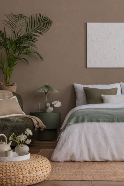 istock Creative composition of bedroom interior with mock up poster frame, braided pouf, plants, gray armchair, stylish lamp, round coffee table, braided rug and personal accessories. Home decor. Template. 2163422840