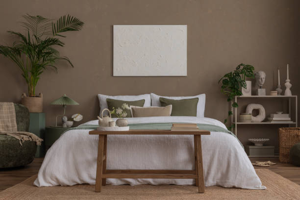 istock Creative composition of bedroom interior with mock up poster frame, braided pouf, plants, gray armchair, stylish lamp, round coffee table, braided rug and personal accessories. Home decor. Template. 2163422971