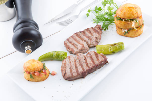 A delicious food presentation: Grilled meat, potato salad, red pepper, green pepper and spices. Taken on a white background. Grilled meat, potato salad and spices create an appetizing image. This photo is perfect for food blogs, restaurant menus or social media posts.