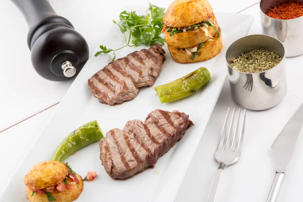 Grilled medium-rare steak with breaded shrimp, vegetables, and a rich red wine sauce, served on a white square plate