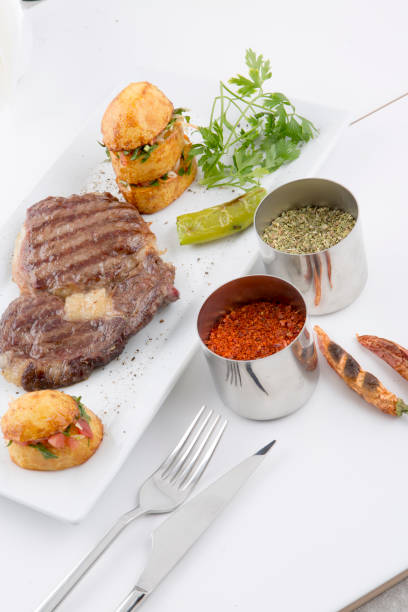 A delicious food presentation: Grilled meat, potato salad, red pepper, green pepper and spices. Taken on a white background. Grilled meat, potato salad and spices create an appetizing image. This photo is perfect for food blogs, restaurant menus or social media posts.