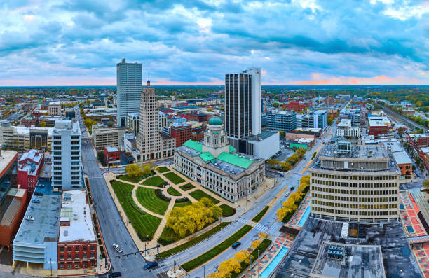 Sweeping aerial view of downtown Fort Wayne, Indiana, with a focus on the historic courthouse at sunset, depicting urban growth and governance
