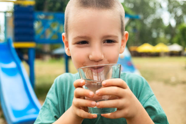 A boy drinks water from a transparent glass on playground