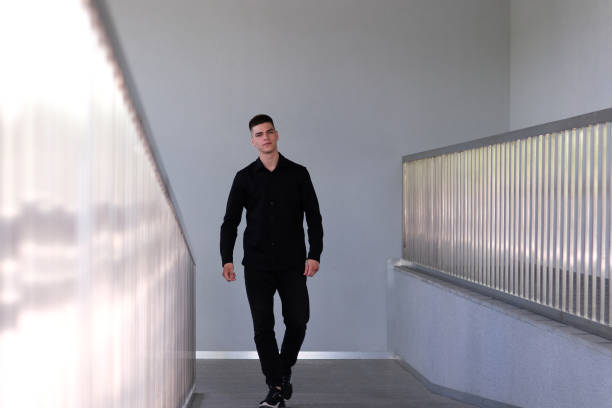 Young businessman going along long office corridor with window corridor back view of camera. Man in business suit clothing walks room hall to meeting work. Office style building success