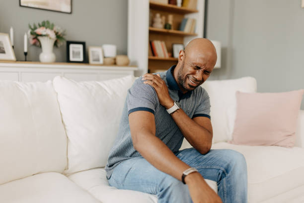 istock Man with shoulder pain sitting on white couch indoors 2163434740