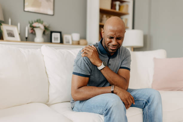 istock Man in pain holding his shoulder on a white sofa. 2163434746