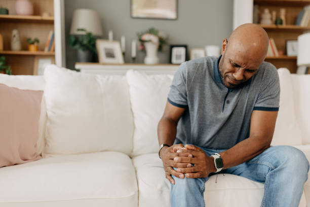 istock Man with knee pain sitting on white couch indoors 2163434870
