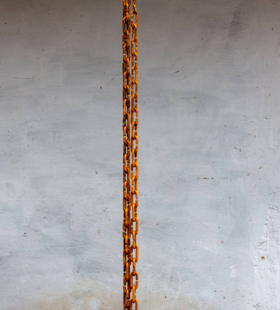 Creative, artistic and minimalist abstraction with a plastic yellow chain hanging vertically. Grey cement background.