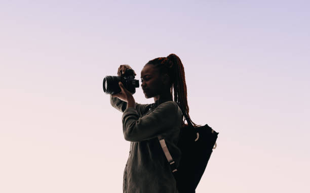 Happy young woman holding a digital camera in a studio, taking pictures with a smile. Young woman showcasing her adventurous lifestyle and photography hobby on a backpacking trip.