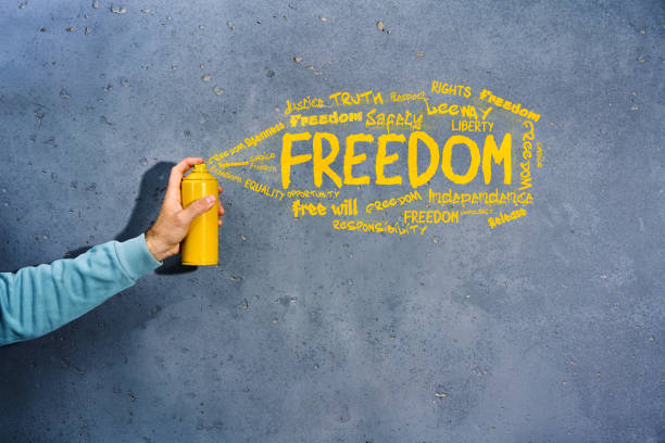 Graffiti painter with spray paint in his hands draws the word FREEDOM and synonyms on concrete wall. Freedom concept