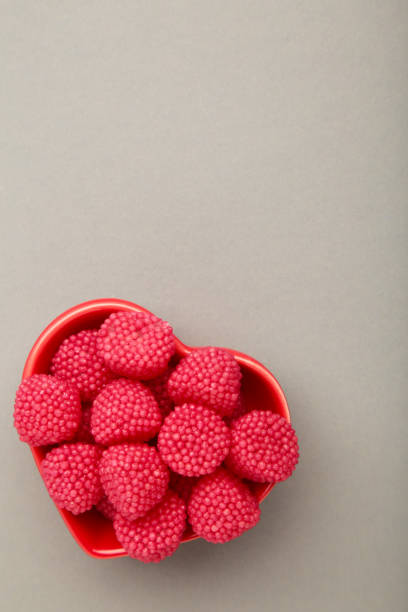 Raspberry and blackberry candy on bowl on grey background. Vertical photo