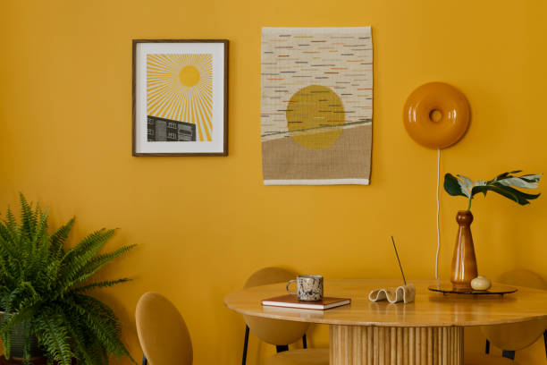 istock Warm and cozy composition of dinning room interior with mock up poster frame, killim rug, round table, yellow chair, wall, vase with leaves, books and personal accessories. Home decor. Template. 2163446473