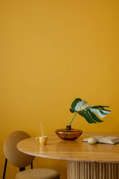 istock Cozy composition of dinning room interior with patterned killim rug, round table, books, cup, plants in flowerpot, orange lamp and personal accessories. Home decor. Template. 2163449392