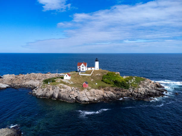 The Nubble Lighthouse at Cape Neddick located on the coast of Maine with rocky terrain in the foreground.