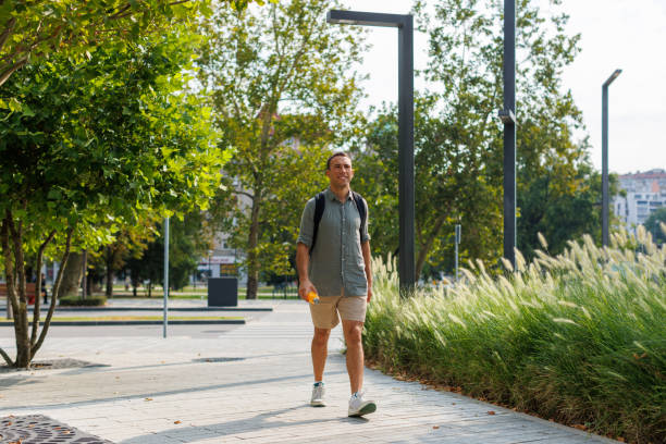 Young Healthy man, walking in the park and drinking supplementation from his sport glass clear bottle.
