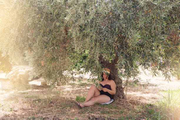 Young woman reading book under olive tree