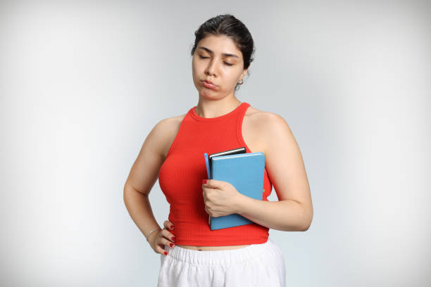 Thoughtful pretty woman looks pensively aside with rounded lips, holds paper folder, has pleasant appearance, being deep in thoughts