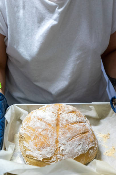 A woman displays a freshly baked loaf of bread.