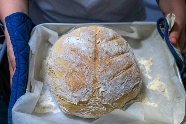 A woman displays a freshly baked loaf of bread.