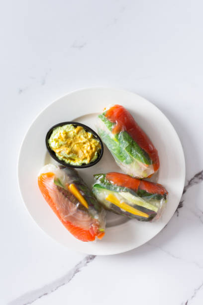 These traditional Vietnamese spring rolls feature rice paper filled with lettuce, salmon, carrots, and cucumber, served with fish sauce, offering a light and flavorful appetizer