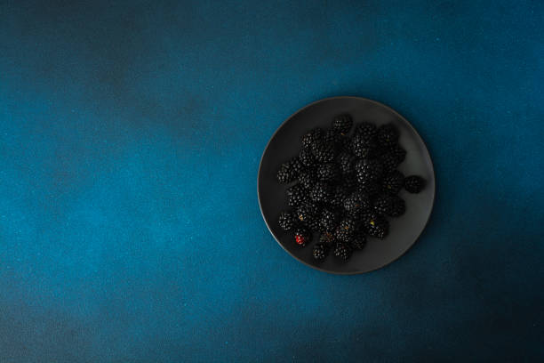 Black plate with blackberries on a dark background. Top view, Copy space.
