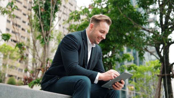 istock Businessman sitting at park while working on tablet by reading report. Urbane 2163489718