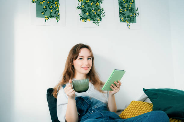 istock Young woman reading e-book on tablet reader in bed. Female relaxing with hot drink while reading an electronic book in cozy room. Mental health recovery, Personal growth. Hobby, Leisure time alone 2163492173