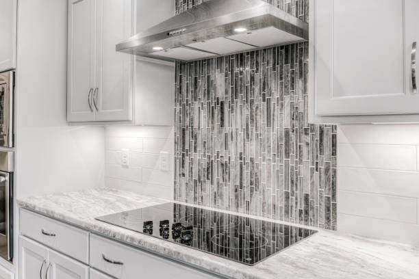 Modern Kitchen With Gray Cabinetry And Chic Tile Backsplash Under Hood Vent.