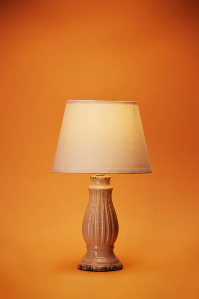 One alone vintage nightstand desk table bedside lamp with empire style shade glowing of soft warm light isolated on the bright solid fond plain orange background