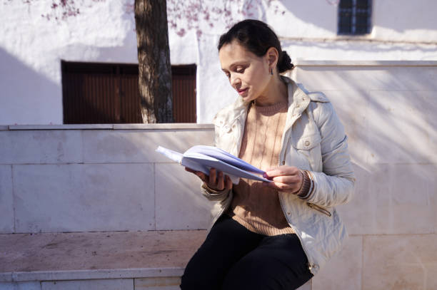 istock Woman reading book outdoors on a sunny day in urban setting 2163521329