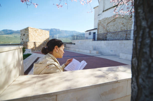 istock Woman reading a book outdoors on a sunny day, surrounded by ancient architecture and scenic landscape 2163521332