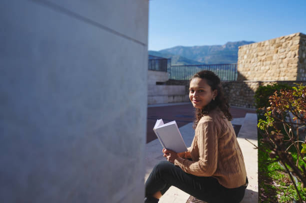 istock Young woman reading a book outdoors on a sunny day in a peaceful setting 2163521351