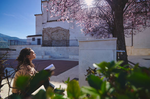 Woman enjoying springtime under a blossoming tree while reading a book in a peaceful outdoor setting
