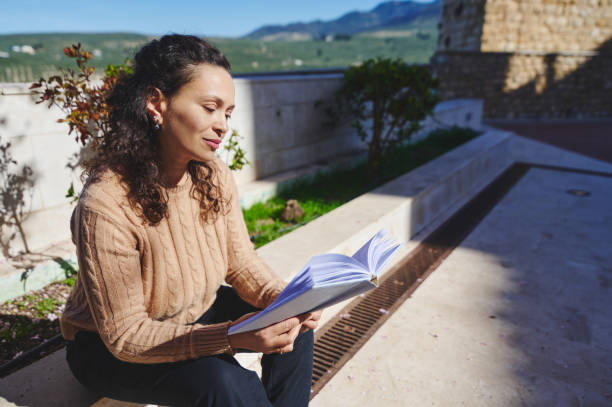 istock Woman relaxing outdoors while reading a book in the sunlight 2163521372