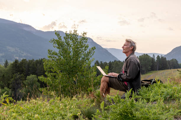 istock Mature man uses laptop in mountain meadow 2163522693