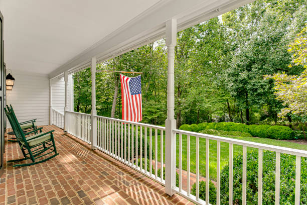 istock Front Patio With Brick Flooring, American Flag, And Green Rocking Chairs 2163522780