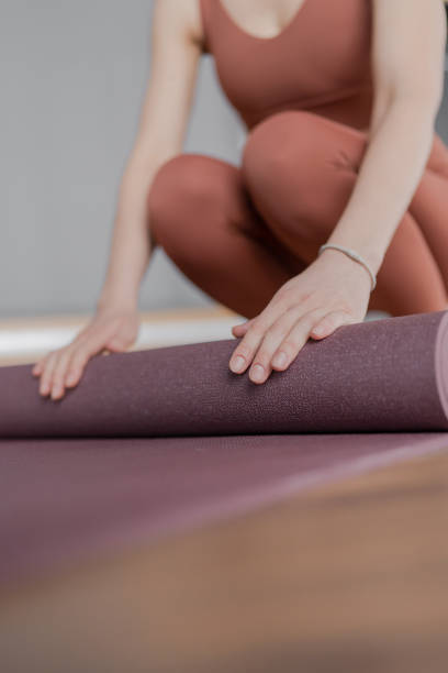 istock Woman trainer rolling out a mat after class. Rolled yoga mats in a studio create a peaceful atmosphere for meditation and exercise. 2163524965