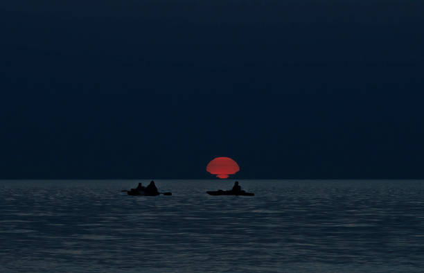 Three kayakers glide across an Ontario lake, silhouetted against the vibrant hues of a setting sun.
