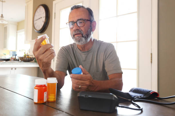 istock Latino Man Sitting At Table Sorting Through Prescription Medications 2163543758