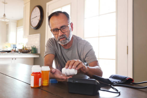 istock Latino Man Sitting At Table Sorting Through Prescription Medications 2163543763
